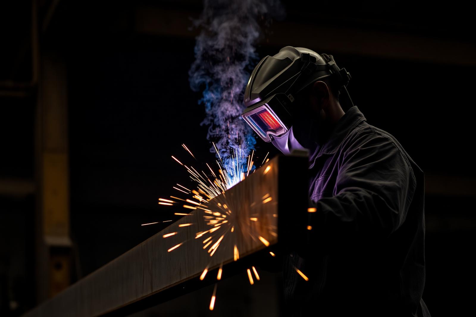 Welder at work on a steel I-beam with sparks